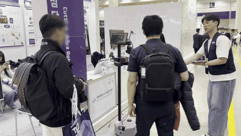 코엑스 부스에서 조끼를 입고 관람객에게 안내 로봇을 시연하는 장면. 로봇 화면에 지도와 주행 로그가 떠 있다